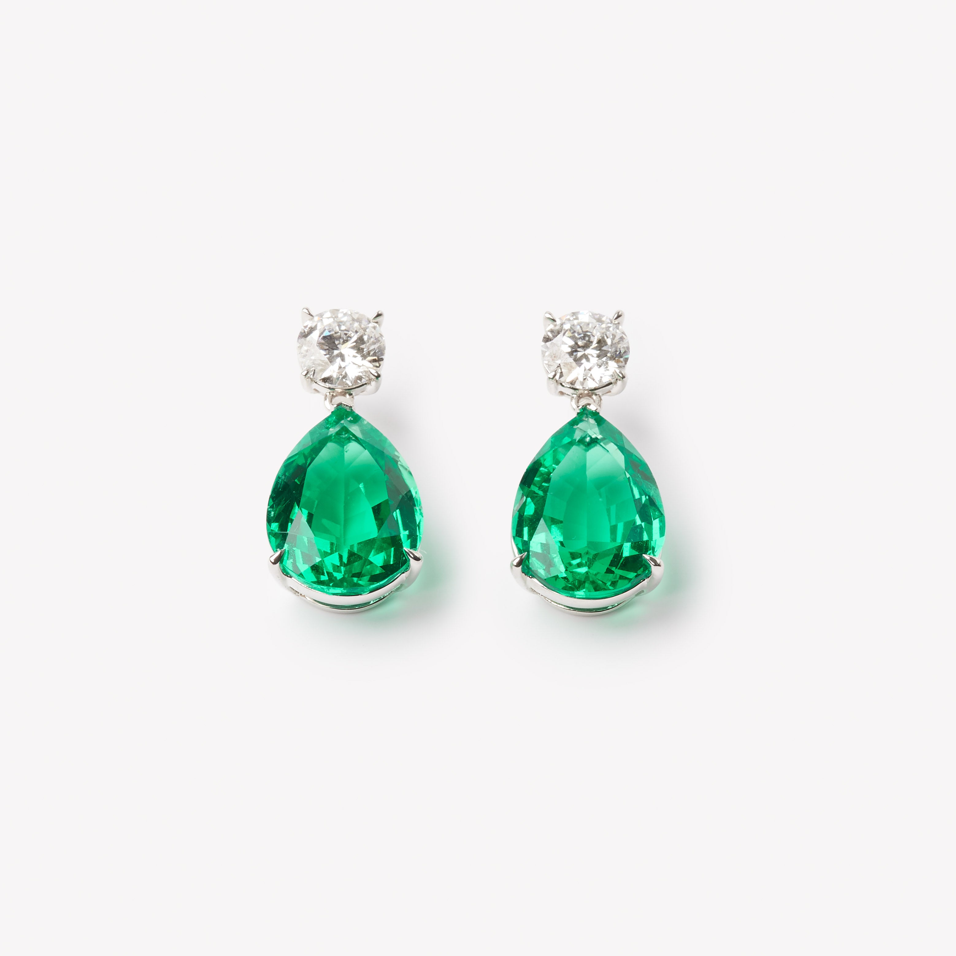 18k gold lab grown diamond and emerald earrings. Round brilliant and pear cut with tiger claw setting.