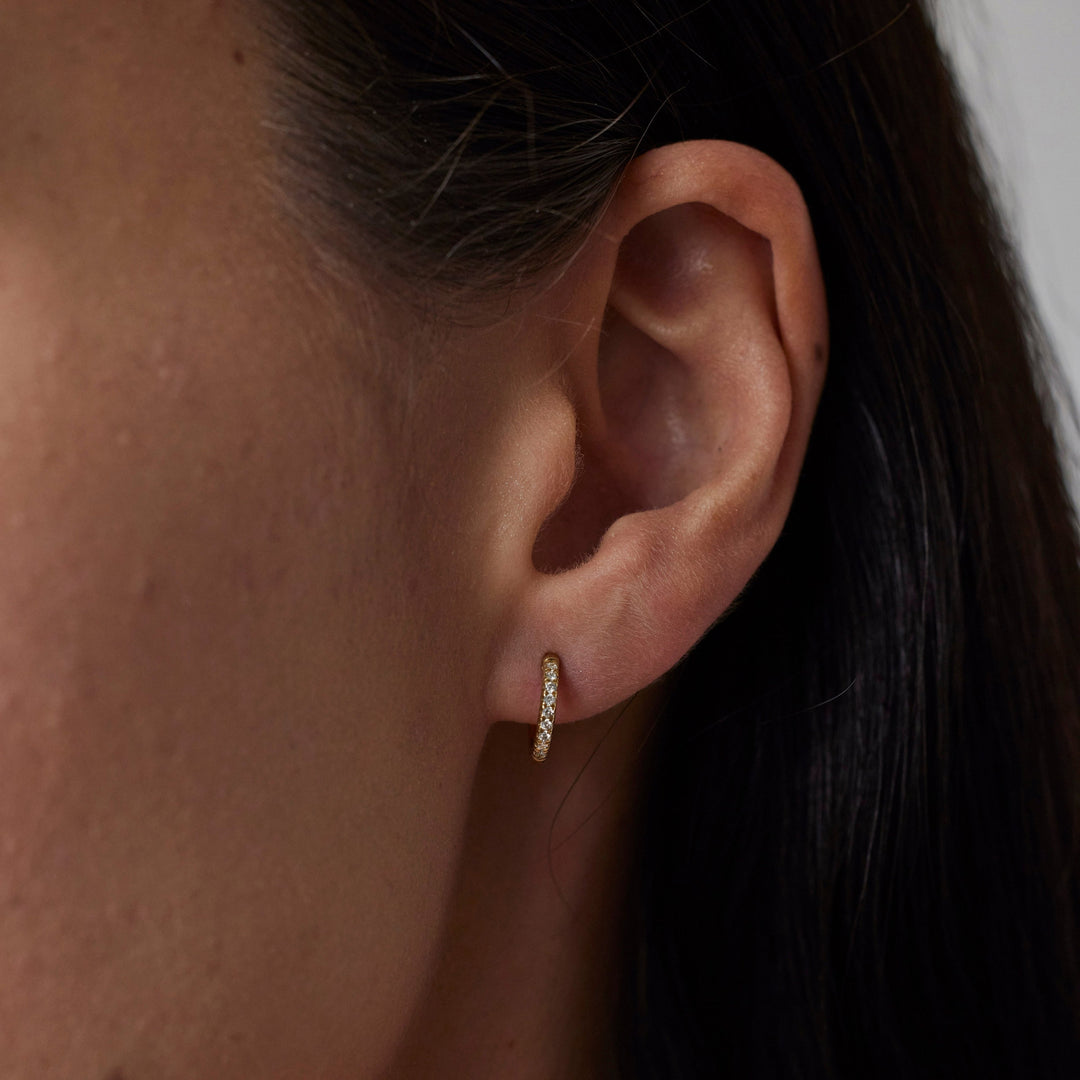 Pair of 18k gold hoop earrings with small lab grown diamonds on model. 0.1 carats of diamonds