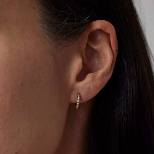 Pair of 18k gold hoop earrings with small lab grown diamonds on model. 0.1 carats of diamonds