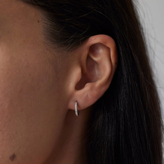 Pair of 18k gold hoop earrings with small lab grown diamonds on model. 0.1 carats of diamonds