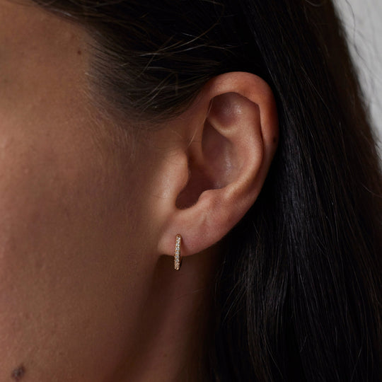 Pair of 18k gold hoop earrings with small lab grown diamonds on model. 0.1 carats of diamonds