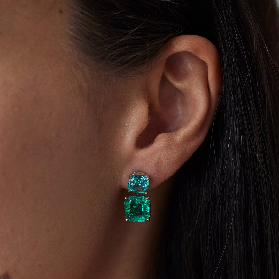 18k gold lab grown emerald and paraiba earrings. Asscher cut with tiger claw prongs. Designed in Zurich. On model