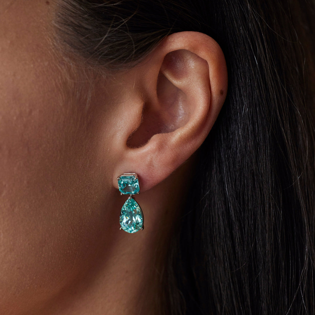 18k yellow gold paraiba earrings. Pear and asscher cut with classic tiger claw setting. On model.