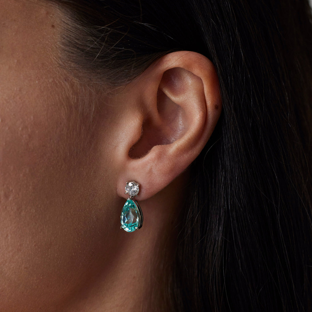 18k gold lab grown diamond and paraiba earrings. Round brilliant and pear cut with tiger claw setting. On model.