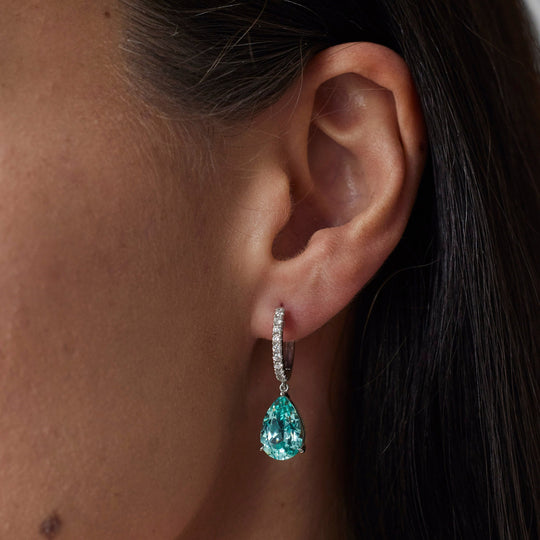 18k gold lab grown paraiba with diamond paved loop. Pear cut in tiger claw setting. On model.